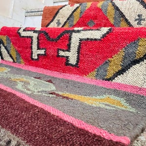 Puede incluir: Un conjunto de alfombras tejidas de colores con patrones geom&eacute;tricos en tonos rojos, rosas, marrones, grises y amarillos. Las alfombras est&aacute;n superpuestas en un tramo de escaleras.