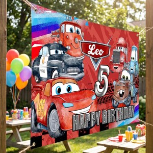 May include: A red and black banner featuring cartoon cars with the text "Leo 5 Happy Birthday." The banner has a red background with a checkered pattern at the bottom. The banner is hanging outside.
