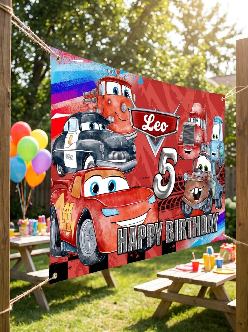 May include: A red and black banner featuring cartoon cars with the text "Leo 5 Happy Birthday." The banner has a red background with a checkered pattern at the bottom. The banner is hanging outside.