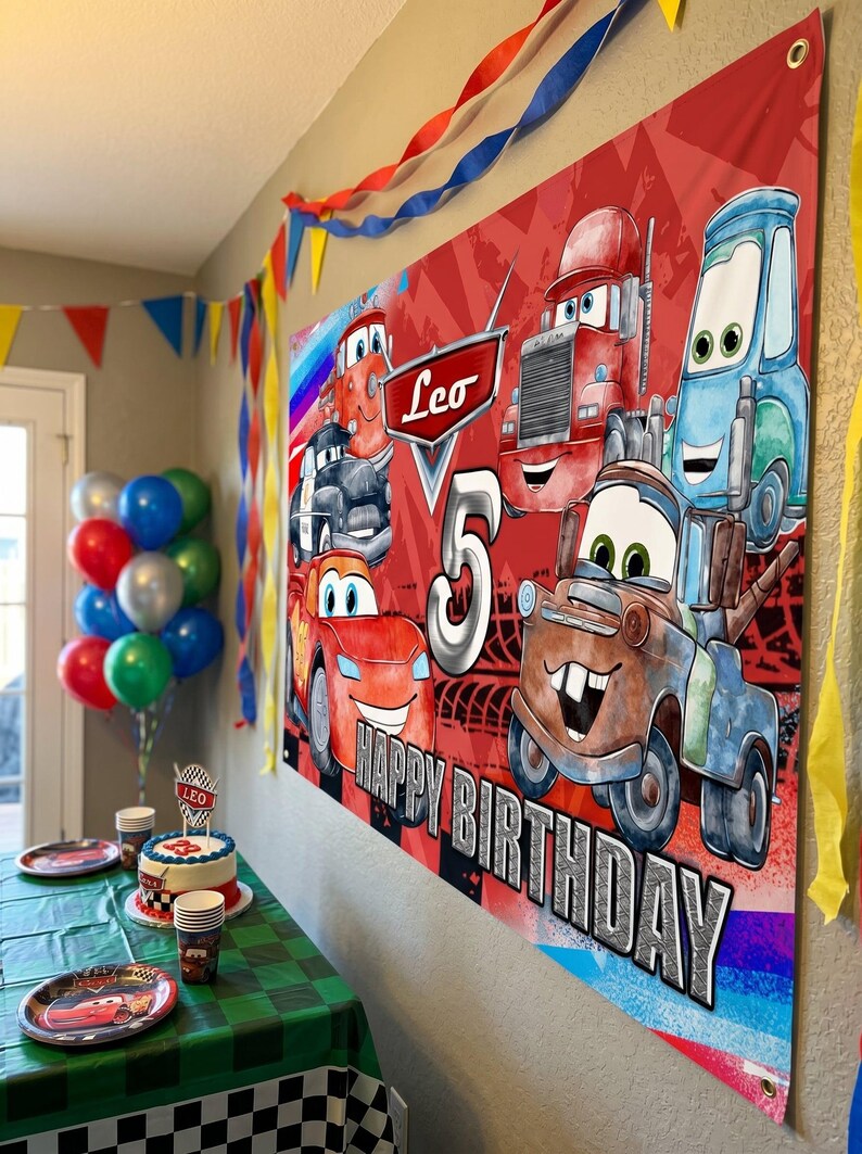 May include: A red banner with cartoon car characters and the text "Leo 5 HAPPY BIRTHDAY" is displayed. The scene includes a decorated table with a cake, plates, and balloons, suggesting a birthday party theme.