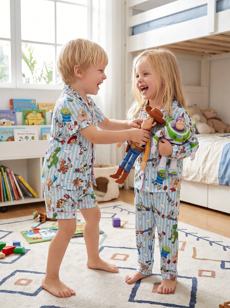 Puede incluir: Dos ni&ntilde;os con pijamas a rayas azules y blancas a juego con estampados de personajes de Toy Story. Un ni&ntilde;o sostiene mu&ntilde;ecos de Woody y Buzz Lightyear. Los pijamas incluyen una camisa de manga corta y pantalones cortos, y una camisa de manga larga y pantalones.