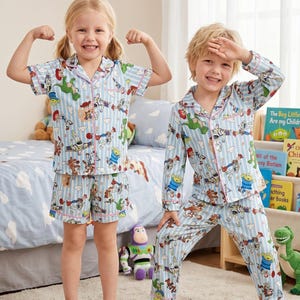 Puede incluir: Dos ni&ntilde;os con pijamas azules a juego con estampado de Toy Story. Los pijamas tienen un patr&oacute;n de rayas verticales y ribetes rosas. Uno lleva una camiseta de manga corta y pantalones cortos, el otro una camiseta de manga larga y pantalones.