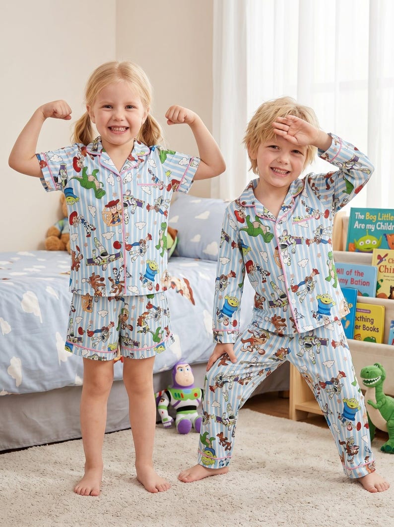 Puede incluir: Dos ni&ntilde;os con pijamas azules a juego con estampado de Toy Story. Los pijamas tienen un patr&oacute;n de rayas verticales y ribetes rosas. Uno lleva una camiseta de manga corta y pantalones cortos, el otro una camiseta de manga larga y pantalones.