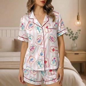 May include: A two-piece pajama set featuring a white and pink striped pattern. The set includes a short-sleeved button-up shirt and shorts, both trimmed with burgundy piping. The fabric is adorned with colorful, illustrated tile motifs.