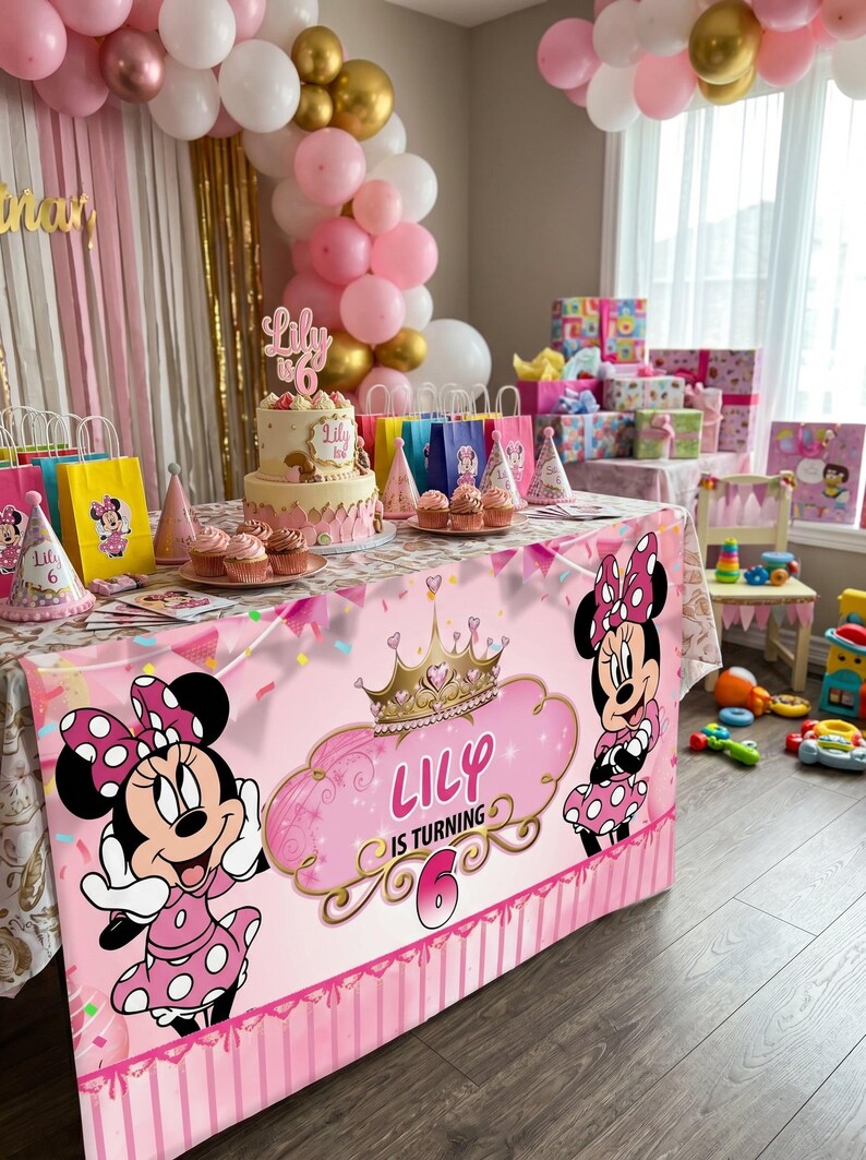 May include: A festive birthday party scene with a pink and gold color scheme. A table is decorated with a Minnie Mouse tablecloth, cake, cupcakes, and party favors. Balloons and gifts complete the celebratory atmosphere. The text on the tablecloth reads "Lily is turning 6."