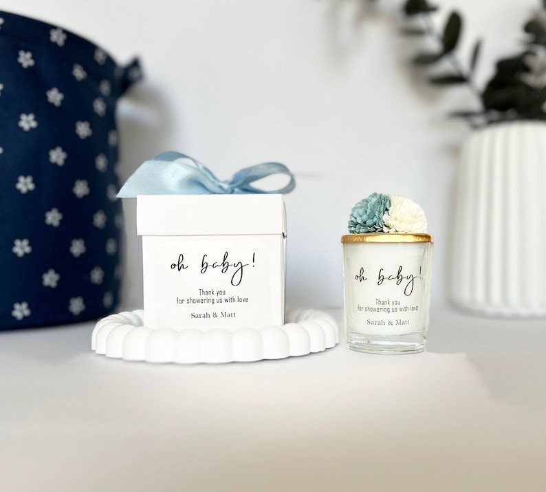 May include: Two white gift boxes with blue ribbon and floral accents. The boxes are labelled "oh baby!" and include the text "Thank you for showering us with love Sarah & Matt".