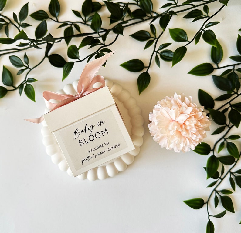 There are colorful artificial flowers on the glass candle made with soy wax. There is a customizable label on the cup.