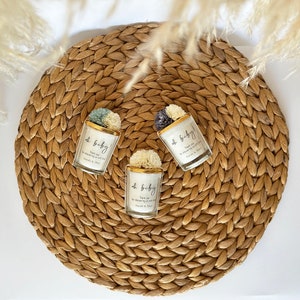 There are colorful artificial flowers on the glass candle made with soy wax. There is a customizable label on the cup.