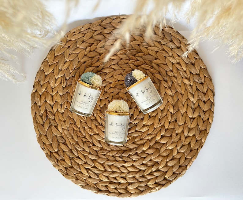 There are colorful artificial flowers on the glass candle made with soy wax. There is a customizable label on the cup.