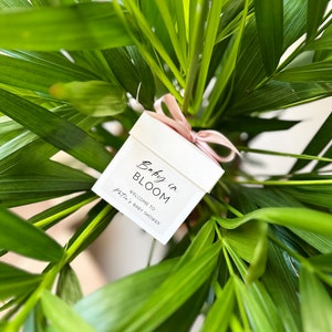 There are colorful artificial flowers on the glass candle made with soy wax. There is a customizable label on the cup.