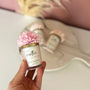 There are colorful artificial flowers on the glass candle made with soy wax. There is a customizable label on the cup.