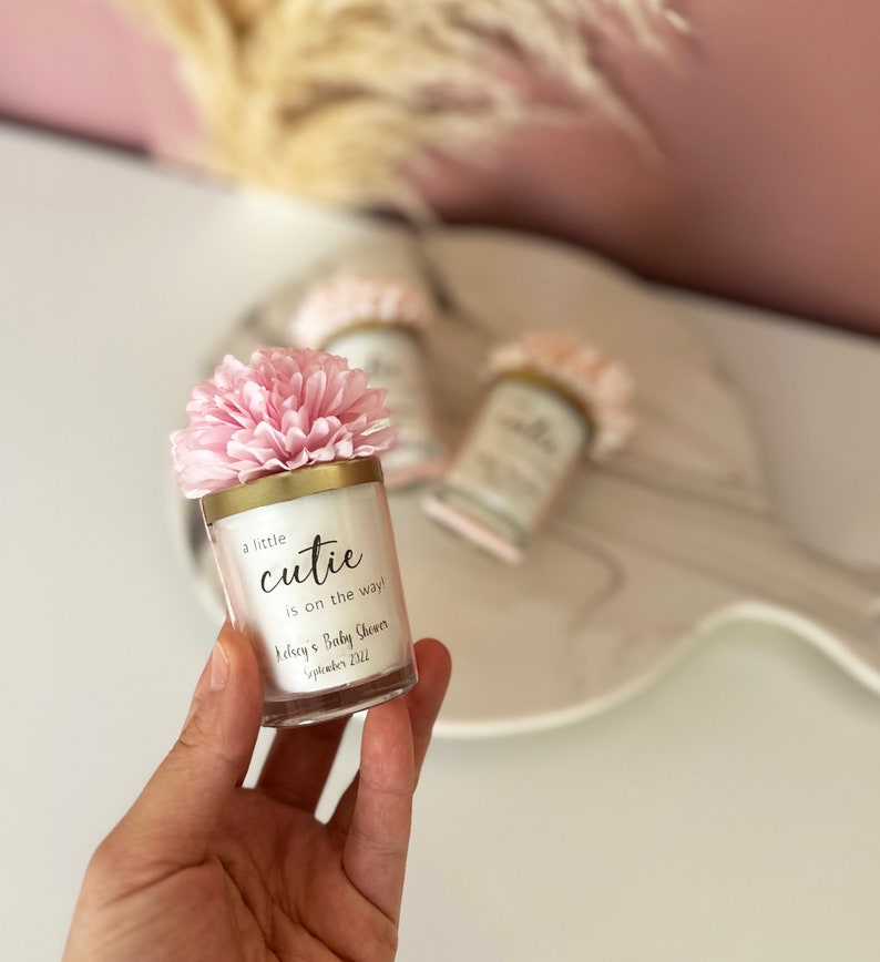 There are colorful artificial flowers on the glass candle made with soy wax. There is a customizable label on the cup.