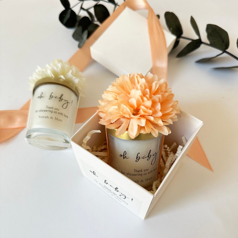 There are colorful artificial flowers on the glass candle made with soy wax. There is a customizable label on the cup.