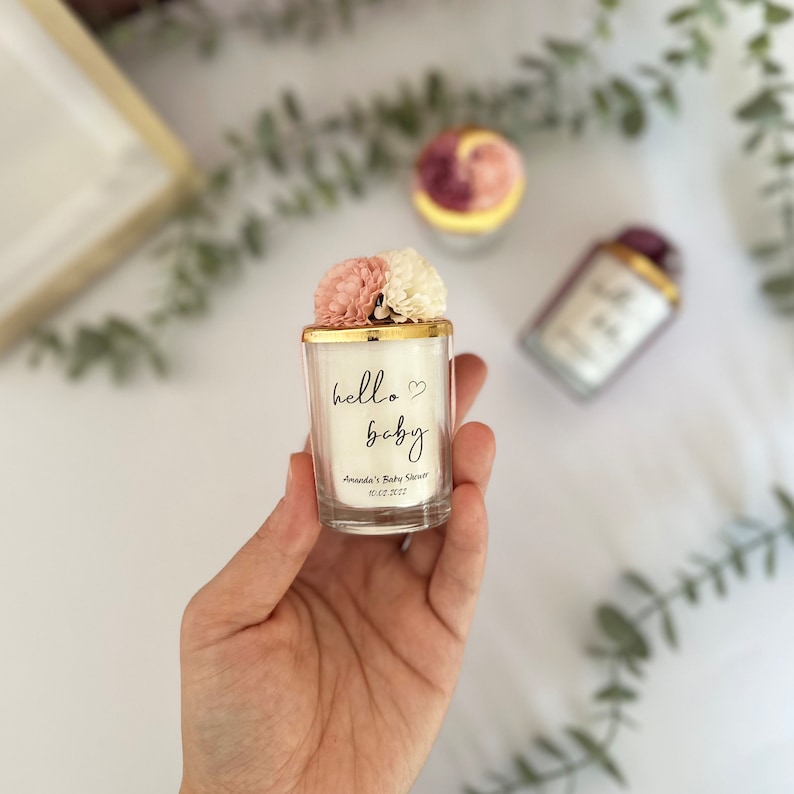 There are colorful artificial flowers on the glass candle made with soy wax. There is a customizable label on the cup.
