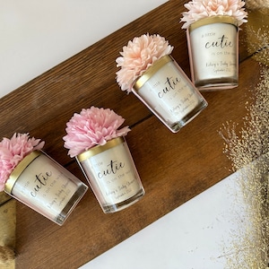 There are colorful artificial flowers on the glass candle made with soy wax. There is a customizable label on the cup.