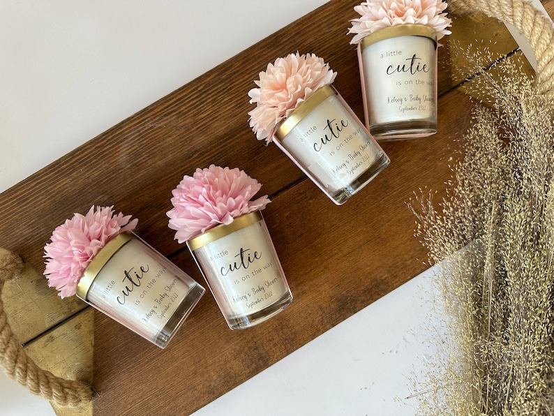 There are colorful artificial flowers on the glass candle made with soy wax. There is a customizable label on the cup.
