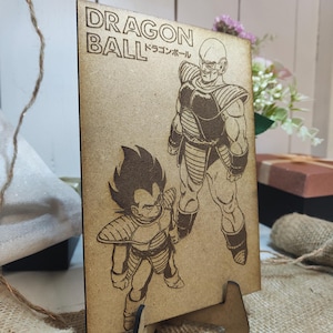 Peut inclure: Une image gravée au laser sur du bois représentant deux personnages de la série d'anime Dragon Ball. Les personnages sont Vegeta et Nappa. L'image est sur une plaque de bois avec le texte "DRAGON BALL ドラゴンボール" en haut.