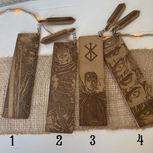 May include: Four wooden bookmarks with engraved illustrations from a manga series. Each bookmark is rectangular with a detailed image of a character. The bookmarks are connected to a small wooden charm with a metal chain. The bookmarks are numbered 1, 2, 3, and 4.