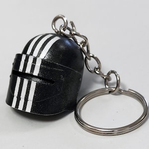 Puede incluir: Llavero de casco negro y blanco a rayas con un anillo y una cadena de metal plateado.