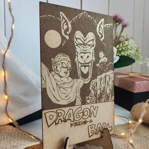 Puede incluir: Una placa de madera con una imagen grabada con l&aacute;ser de un personaje de la serie de anime Dragon Ball. El personaje est&aacute; en un estado transformado con una cara grande y amenazante. El texto "Dragon Ball" y los caracteres japoneses para "Dragon Ball" tambi&eacute;n est&aacute;n grabados en la placa.