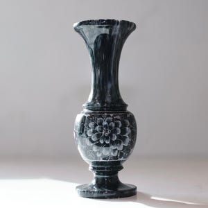 May include: A dark gray marble vase with a flared top and a round base. The vase features a floral design carved around the middle. The vase is approximately 10 inches tall.