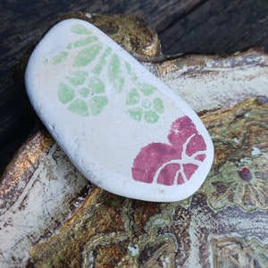Peut inclure: Une pierre blanche avec un motif floral vert et un motif en forme de cœur rouge.