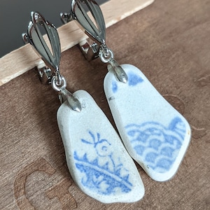 May include: A pair of silver clip-on earrings with blue and white porcelain pendants. The pendants feature a floral design and a wave pattern.