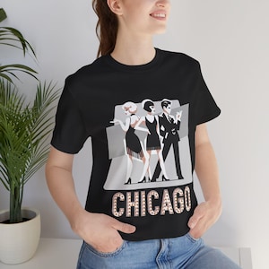 Puede incluir: Camiseta negra con un gráfico de tres personas en blanco y negro, con la palabra "CHICAGO" en pedrería debajo del gráfico.
