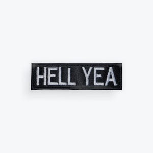 May include: Black rectangular patch with the embroidered text "HELL YEA" in white. The patch has a black border and is set against a white background. The patch is a simple, bold statement.