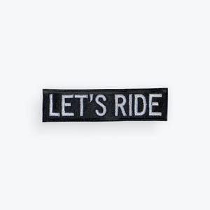 May include: Black rectangular patch with the text "LET'S RIDE" embroidered in white. The patch is likely designed to be sewn or ironed onto clothing or accessories.