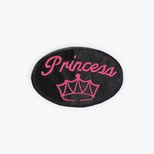 May include: Black oval patch with the word "Princess" embroidered in pink script above a pink crown design. The patch is a simple, yet elegant accessory.