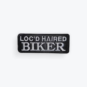 May include: Black rectangular patch with the words "LOC'D HAIRED BIKER" embroidered in white. The patch has a black border and is likely designed to be sewn onto clothing or accessories.