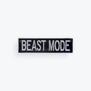 May include: A black rectangular patch with the words "BEAST MODE" embroidered in white. The patch is a simple, bold design, suitable for application on clothing or accessories.