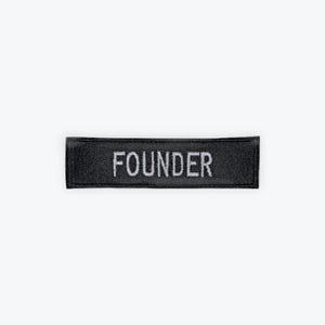 May include: A black rectangular patch with the word "FOUNDER" embroidered in white capital letters. The patch is likely made of a durable fabric and is designed to be sewn or attached to clothing or accessories.