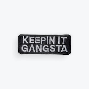 May include: Black rectangular patch with the phrase "KEEPIN IT GANGSTA" embroidered in white. The patch has a black border and is centered on a white background. The text is in a bold, sans-serif font.