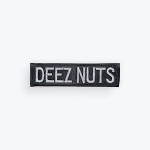 May include: A black rectangular patch with the words "DEEZ NUTS" embroidered in white. The patch has a white border and is set against a white background.
