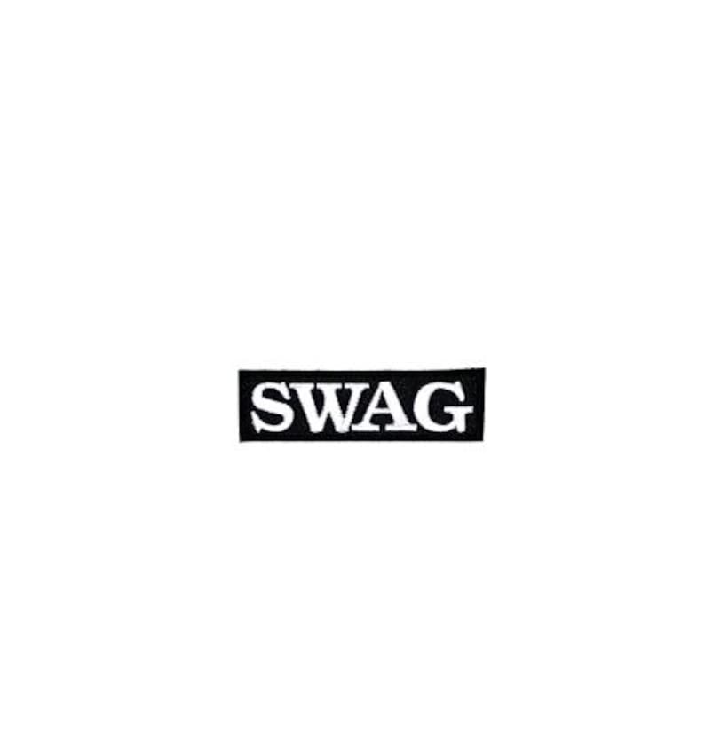 Może przedstawiać: Czarna prostokątna naszywka z napisem "SWAG" w białych, pogrubionych, wielkich literach. Naszywka jest wyśrodkowana na białym tle. Naszywka jest prawdopodobnie przeznaczona na odzież lub akcesoria.