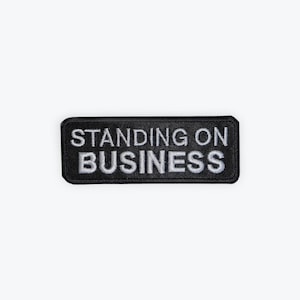 May include: Black rectangular patch with the words "STANDING ON BUSINESS" embroidered in white. The patch has a black border and is set against a white background.