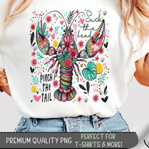 May include: A white t-shirt with a colorful lobster illustration. The lobster is surrounded by flowers, hearts, and lemons. The text "Suck the head" and "Pinch the tail" is written on the shirt.