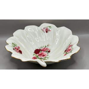 May include: A white porcelain bowl shaped like a large leaf with scalloped edges and a gold-trimmed rim. The interior features clusters of pink and deep red roses with green leaves painted in the center and along the curved, fluted sides.
