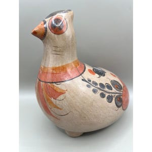 May include: A ceramic bird figurine with a cream-colored body, featuring orange, red, and black painted details. The bird has large, round eyes, a pointed beak, and decorative floral patterns on its body. The figurine is a decorative item.