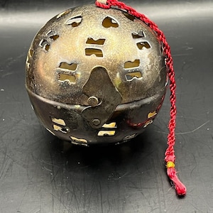 May include: A silver-colored, spherical decorative object with cut-out patterns. It has a hinged opening and a red cord attached. The object appears to be made of metal and has a vintage or antique aesthetic.