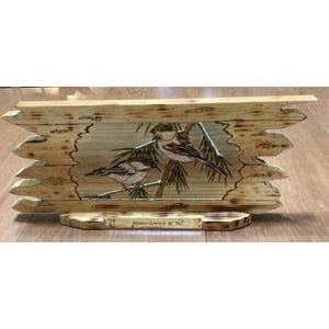 May include: Wooden wall art featuring a painting of two birds perched on a branch. The artwork is framed by a rustic, light-colored wooden border with a decorative edge. The text "HERE'S LOOKIN AT YA!" is visible.