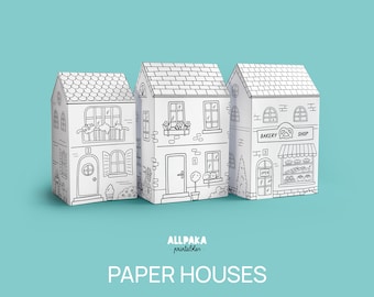May include: Three black and white printable paper houses with a bakery shop, a house with a window box, and a house with a window box and shutters. The houses are on a light blue background. The text "ALLPAKA printable" and "PAPER HOUSES" is below the houses.