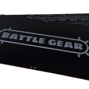 May include: Two black rectangular game mats with the words "BATTLE GEAR" in gray, along with other gray graphics. The mats are designed for tabletop gaming, with a white background.