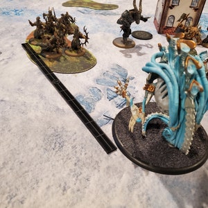 Puede incluir: Una escena de juego de mesa con figuras en miniatura y terreno. La escena incluye varias criaturas de fantas&iacute;a, una herramienta de medici&oacute;n y un tablero de juego detallado con un paisaje nevado.