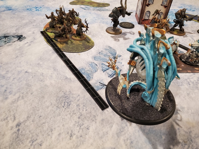 Puede incluir: Una escena de juego de mesa con figuras en miniatura y terreno. La escena incluye varias criaturas de fantas&iacute;a, una herramienta de medici&oacute;n y un tablero de juego detallado con un paisaje nevado.