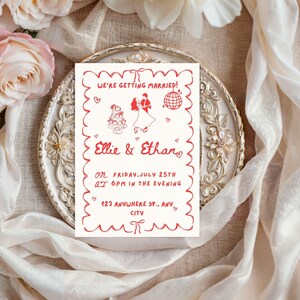 Op de afbeelding: Een trouwuitnodiging met een rode geschulpte rand en tekst. De uitnodiging luidt "We're Getting Married!" en bevat de namen "Ellie & Ethan", datum, tijd en adres. Het ontwerp bevat illustraties van een taart, dansend stel en discobal.