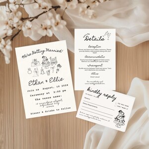 Op de afbeelding: Huwelijksuitnodigingsset met een witte achtergrond en zwarte tekst. De uitnodiging bevat een handgetekende illustratie van een bruidstaart, ringen en champagne glazen. De tekst luidt "We're Getting Married!" gevolgd door de namen van het paar, de datum, tijd en locatie van de ceremonie. De RSVP-kaart bevat een selectievakje voor gasten om hun aanwezigheid aan te geven.