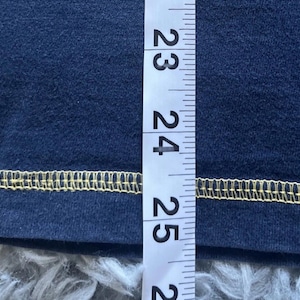 K&ouml;nnte beinhalten: Nahaufnahme eines marineblauen Stoffes mit gelbem Saum. Ein Lineal wird vertikal entlang des Stoffes platziert und zeigt Messungen von 58 bis 63 cm.